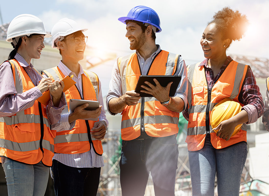 Employee Benefits - Small Group of Cheerful Contractors Standing on a Construction Jobsite Reviewing Building Plans with a Structural Engineer Holding a Tablet